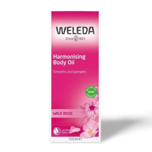 A product packaging of WELEDA Harmonising Body Oil with an image of wild roses on it. The packaging is pink with product information and branding.