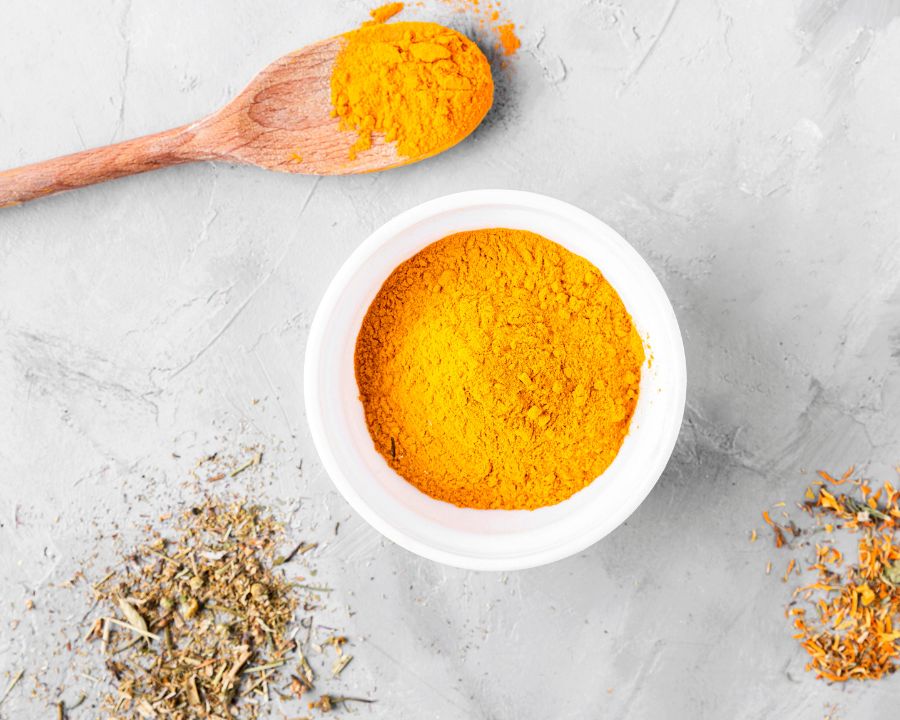 Bright turmeric curcumin powder in a white bowl with wooden spoon — Curcumin Supplements collection by The Good Stuff.