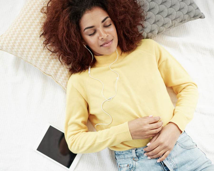 Woman relaxing in yellow jumper with headphones and tablet nearby – Digestive Enzyme Supplements – The Good Stuff