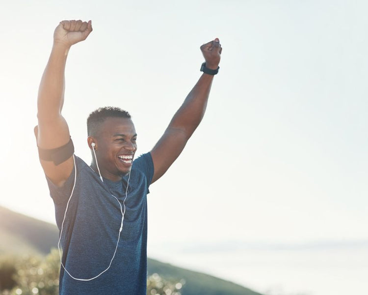 Energy Boost Supplements - The Good Stuff – smiling runner with earphones raising arms outdoors, symbolising energy and vitality