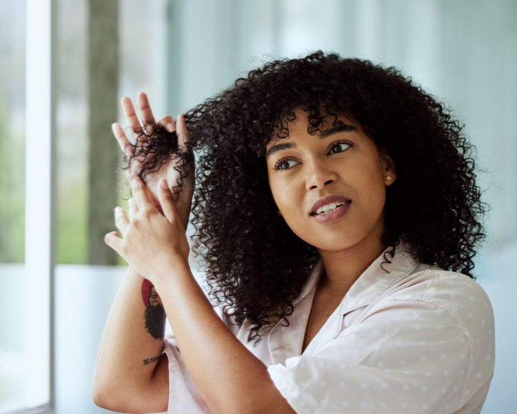 Woman applying hair product to curly hair, showcasing hair growth products in South Africa from The Good Stuff