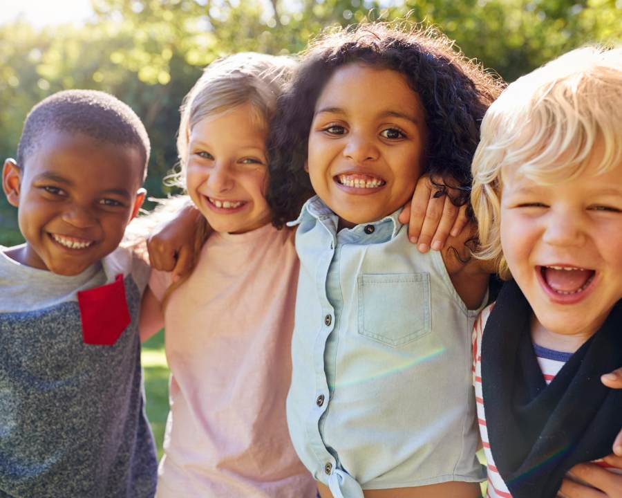 Kid's Supplements - The Good Stuff – happy diverse children hugging outdoors; daily vitamins for minds and bodies.
