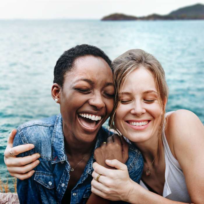 Two women smiling and embracing near the ocean, symbolising the wellness and relaxation benefits of magnesium supplements.