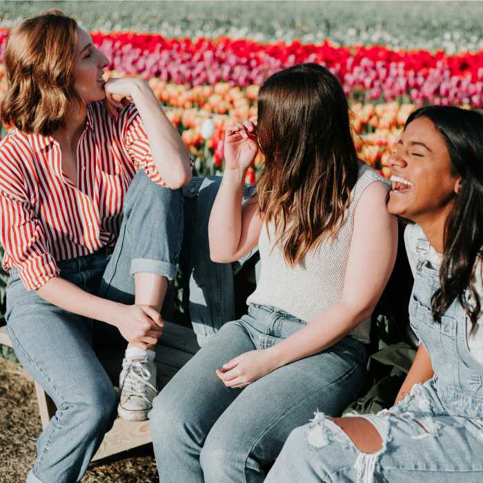 Three friends laughing and chatting together outdoors in front of a vibrant flower field, symbolising the health benefits and joy associated with Omega 3 fatty acids supplements from The Good Stuff.