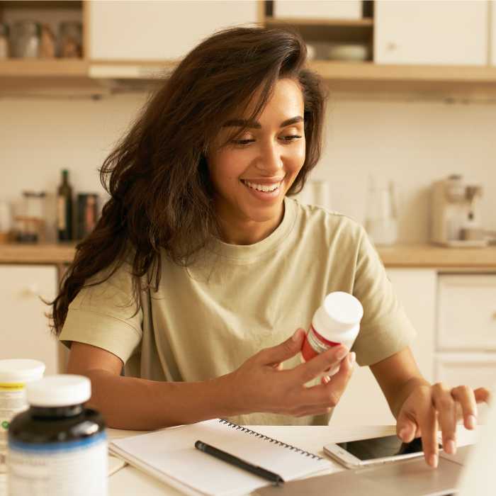 Smiling woman reviewing supplement bottle in kitchen - Organic Store - The Good Stuff.