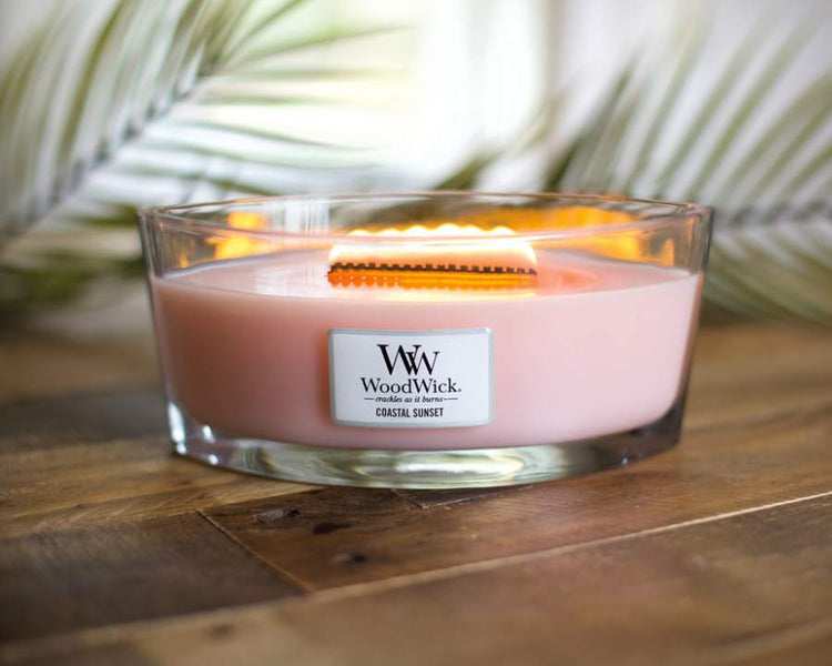 WoodWick Coastal Sunset Candle from The Good Stuff – pink wax in a glass jar with a crackling wooden wick on a wooden table.